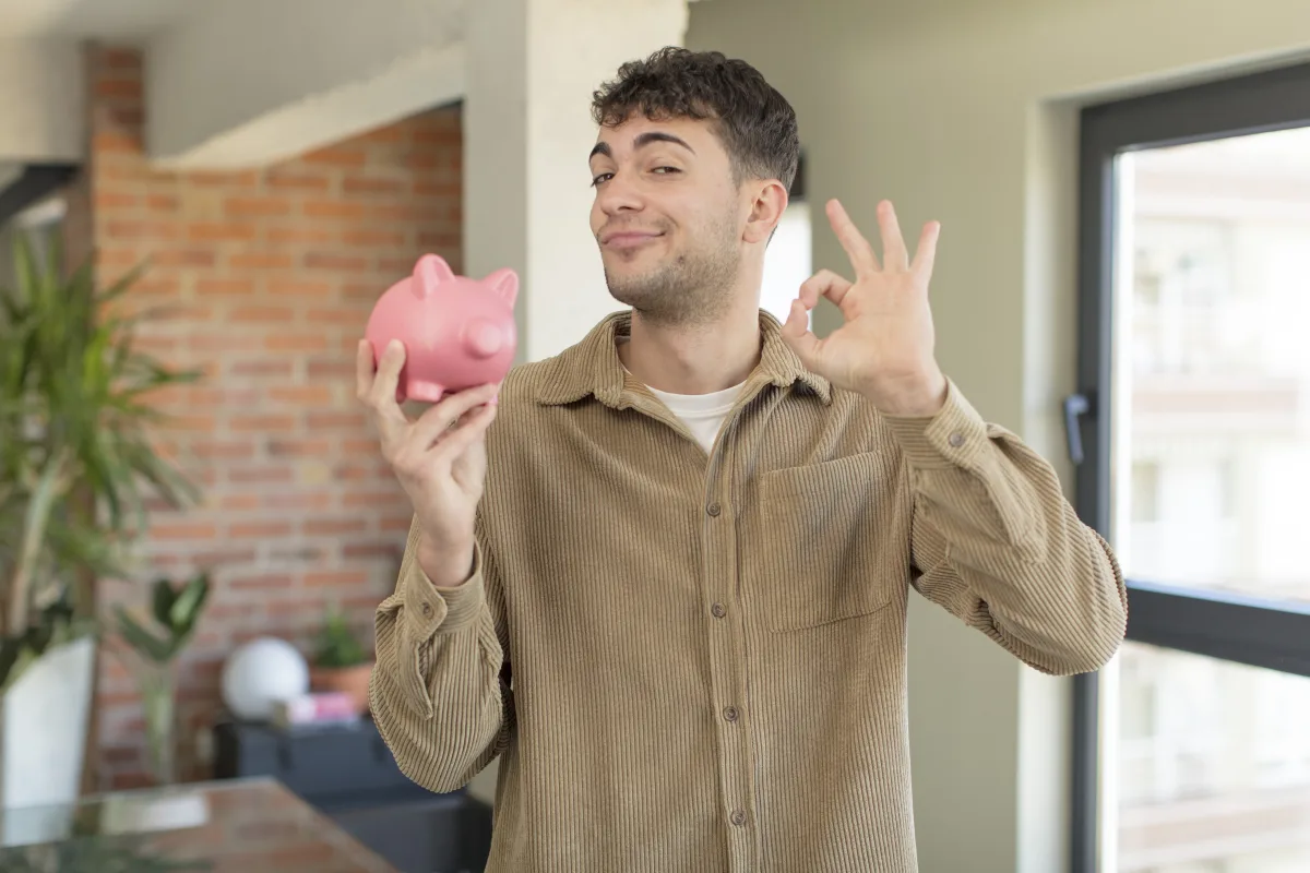 Individual Savings Account: young handsome man feeling happy, showing approval with okay gesture. piggy bank concept